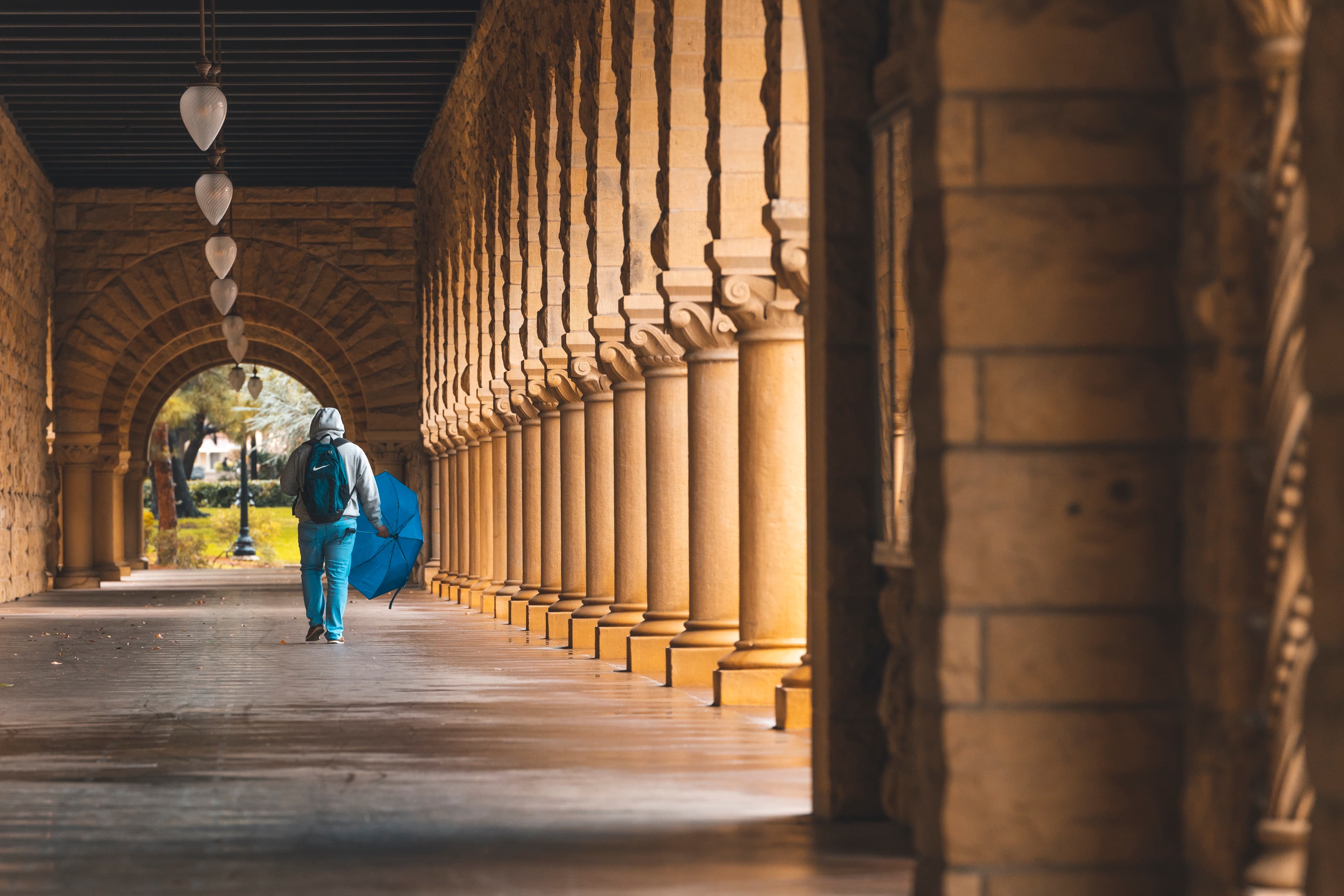 Man walking with umbrella in main quad arcade