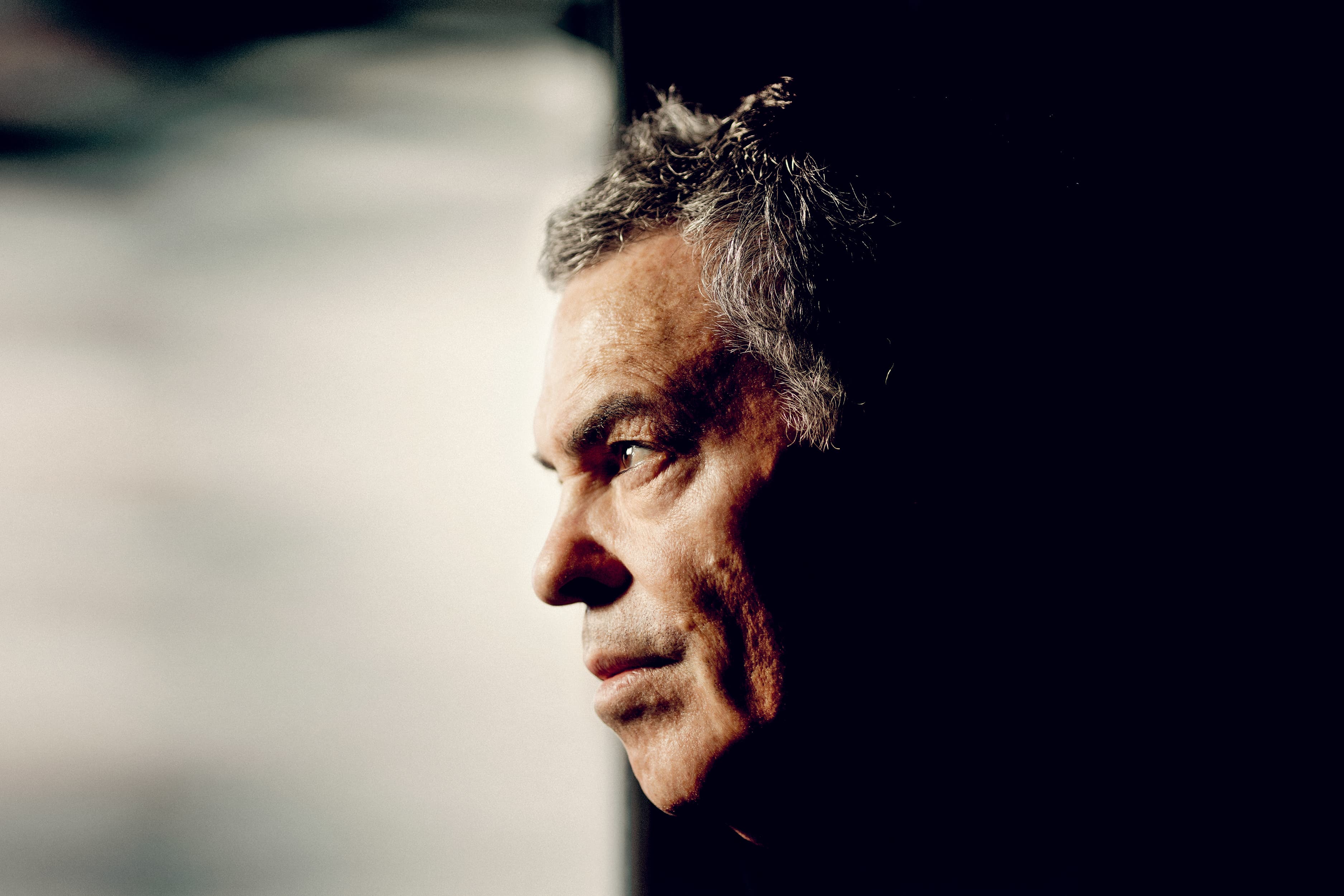 Profile portrait of the filmmaker Amos Gitai against a black and white backdrop.